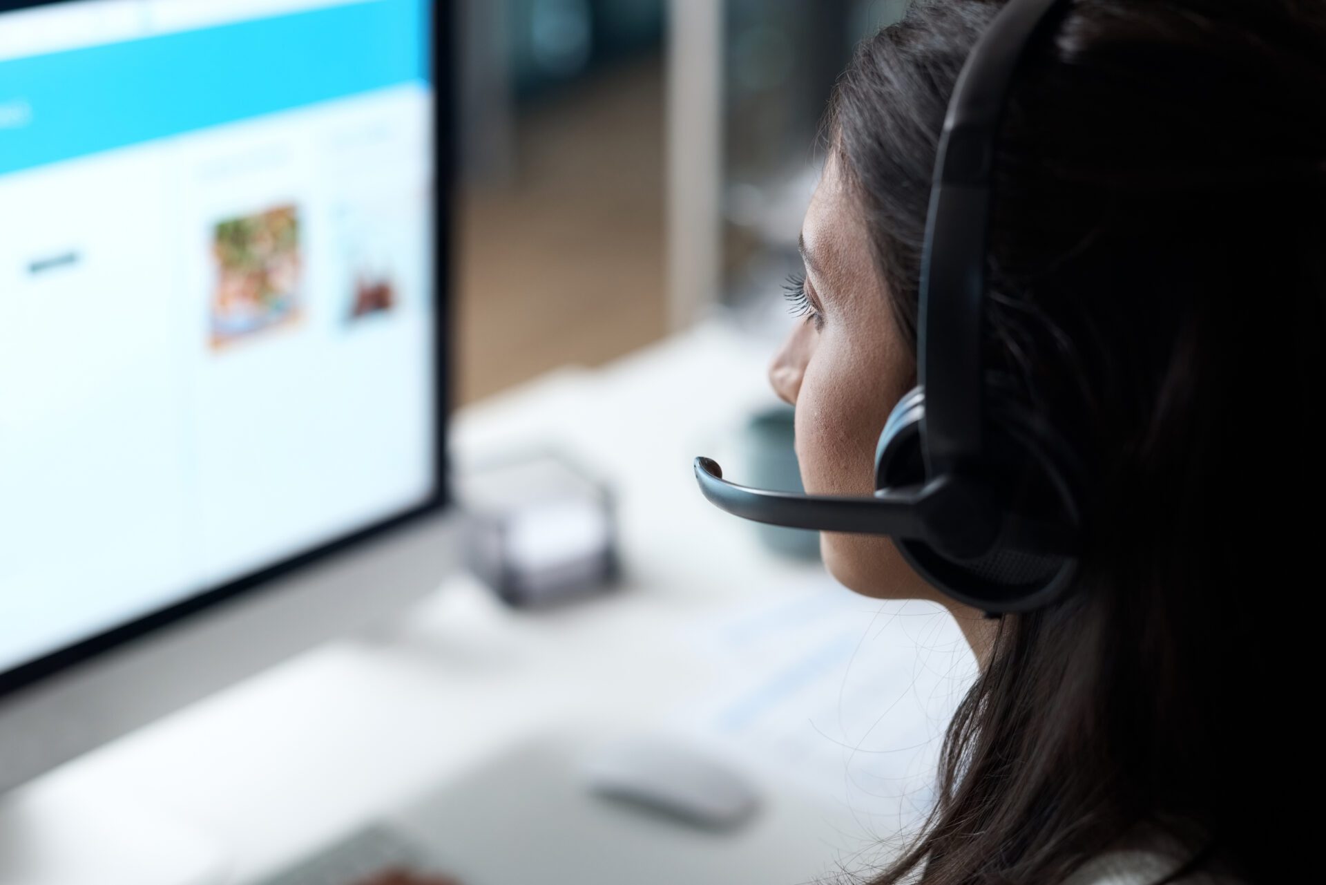 A female telecare service provider sat with an over ear headset looking at a computer screen.